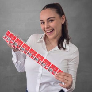 Ilona Züger, Mitglied des Team WILUX PRINT und technischer Verkäuferin in der Abteilung Media, hält eine Etikettenrolle in den Händen, professionell gekleidet in einem weissen Hemd vor einem neutralen Hintergrund.
